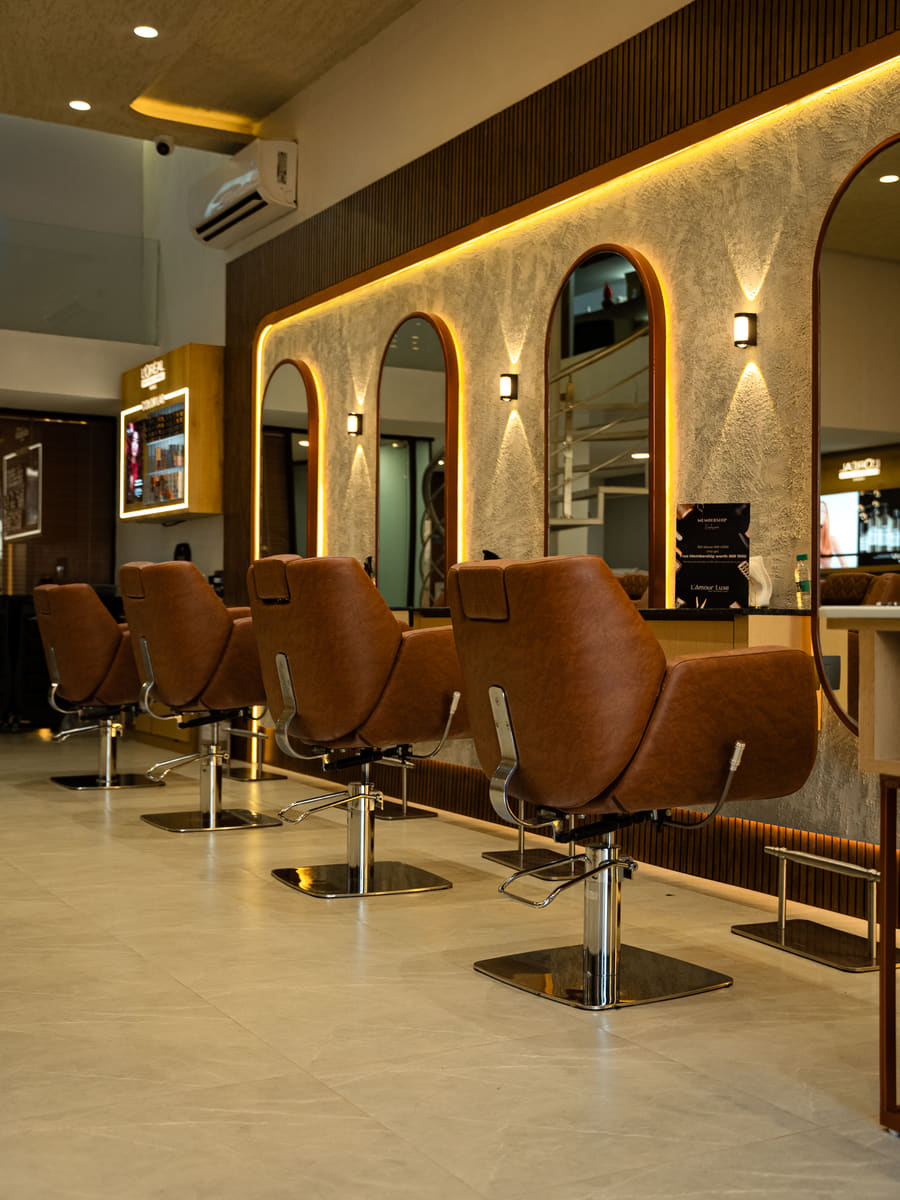 Four tan leather styling chairs in a row down the length of the salon, each facing an arch-topped mirror lit from behind.