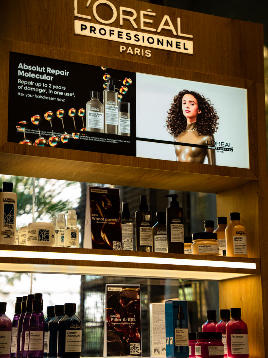 Backlit retail shelving holding L'Oréal Professionnel and Kérastase bottles beneath an illuminated brand panel.