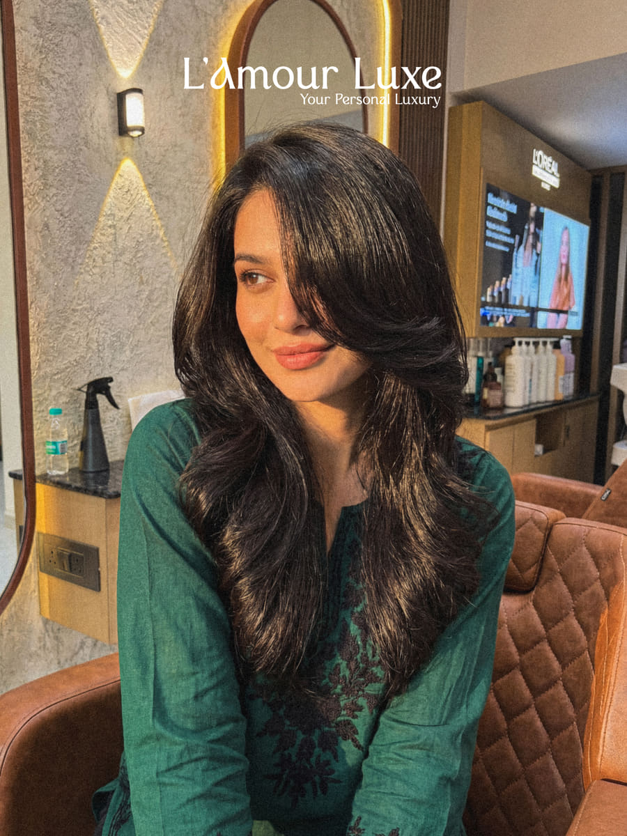A client seated in the salon after a cut and finish, long dark hair in soft layers falling past the shoulder.