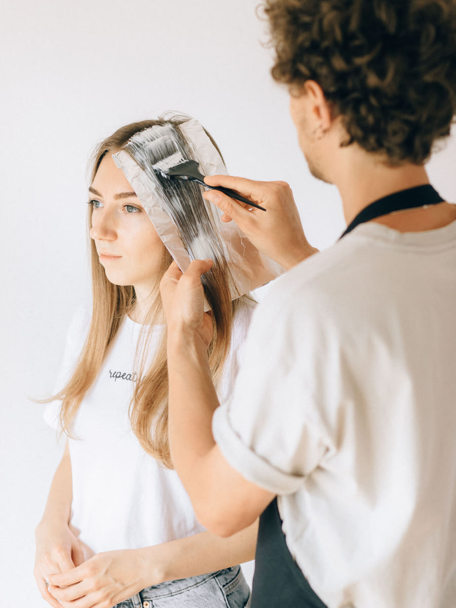 A colourist applying tint through the mid-lengths of a client's hair with a brush in a salon.