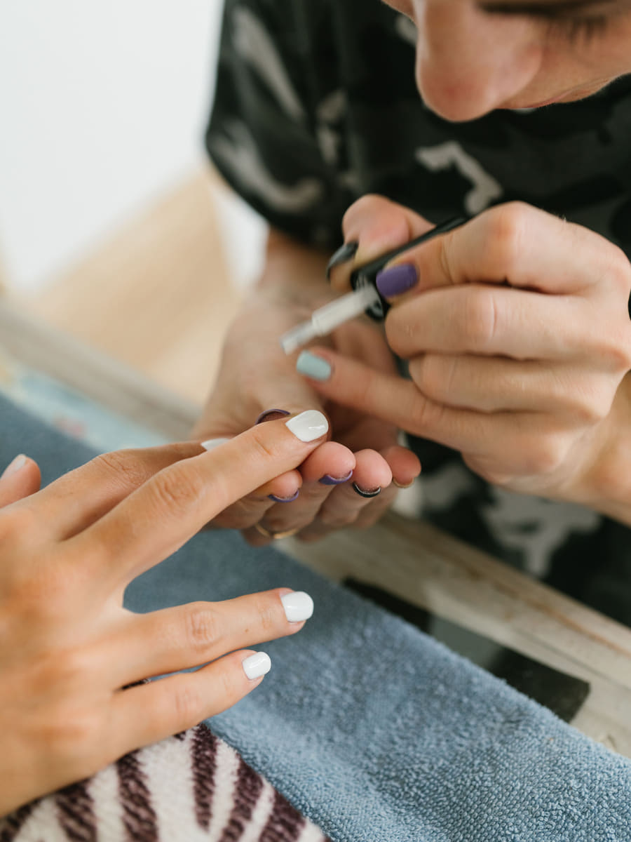 A technician painting a client's nails with a fine brush, both hands resting on a folded towel.