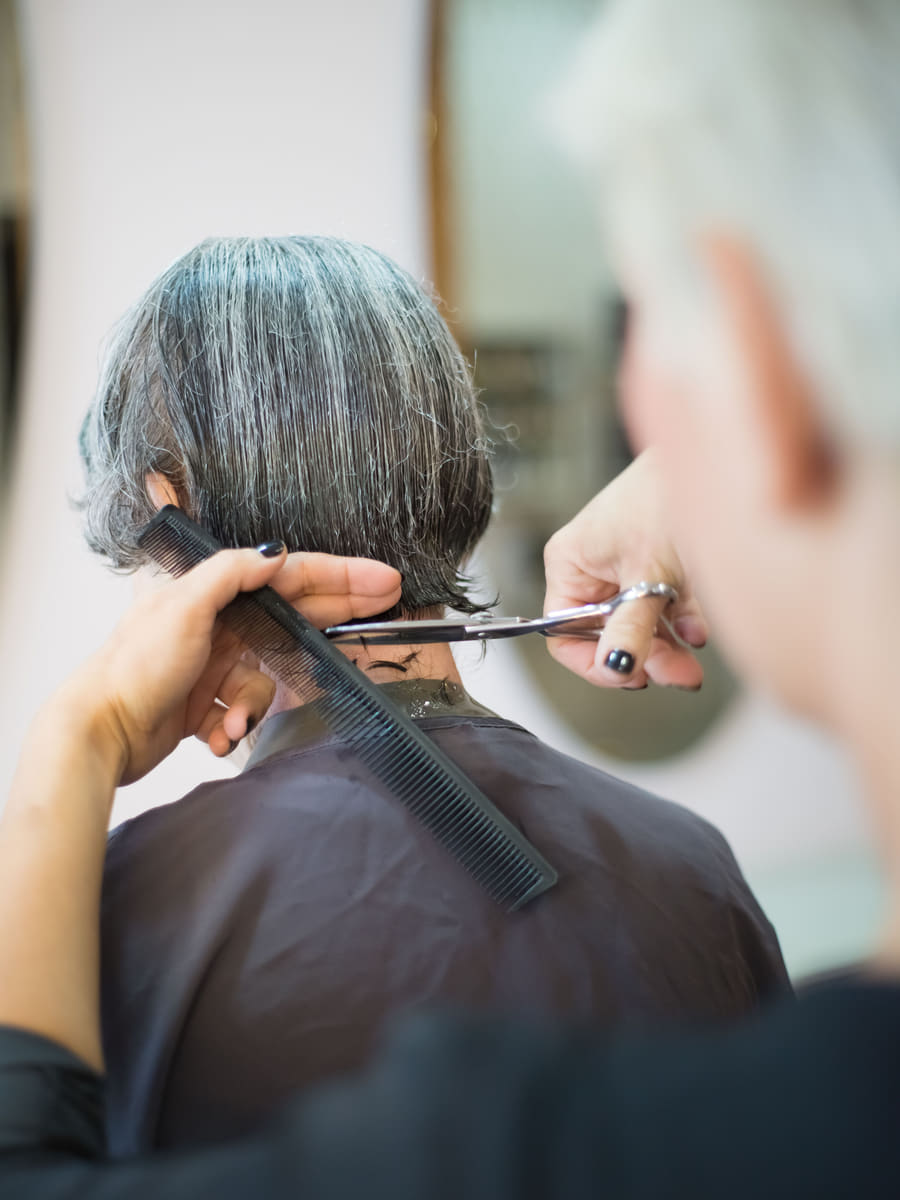 A stylist cutting into the nape with scissors over a comb, the client's hair sectioned and damp.